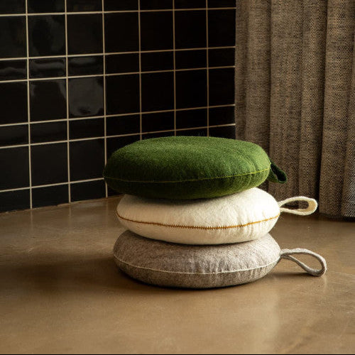 Three stacked cushions on a wooden floor with a black tiled wall and brown curtain in the background.