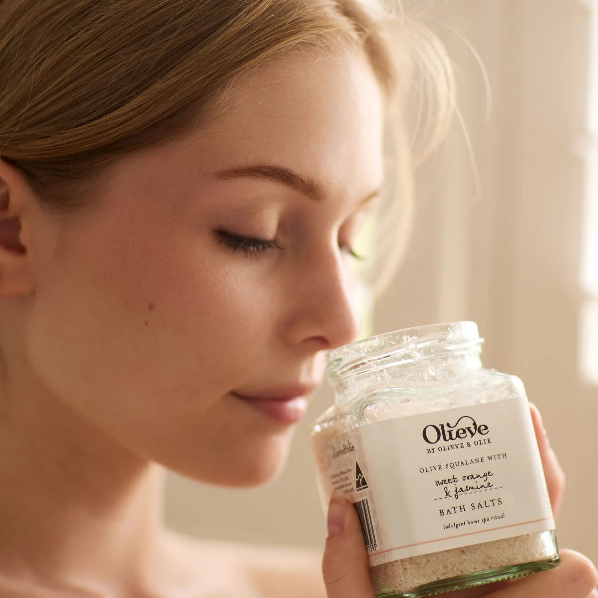Woman holding a jar of Olive & Fig bath salts with a blurred background
