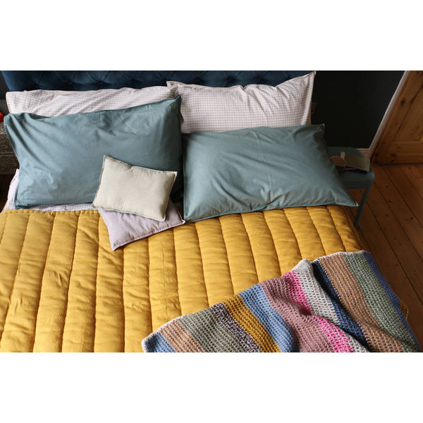Camomile London Quilted Cotton Blanket | ochre - on bed