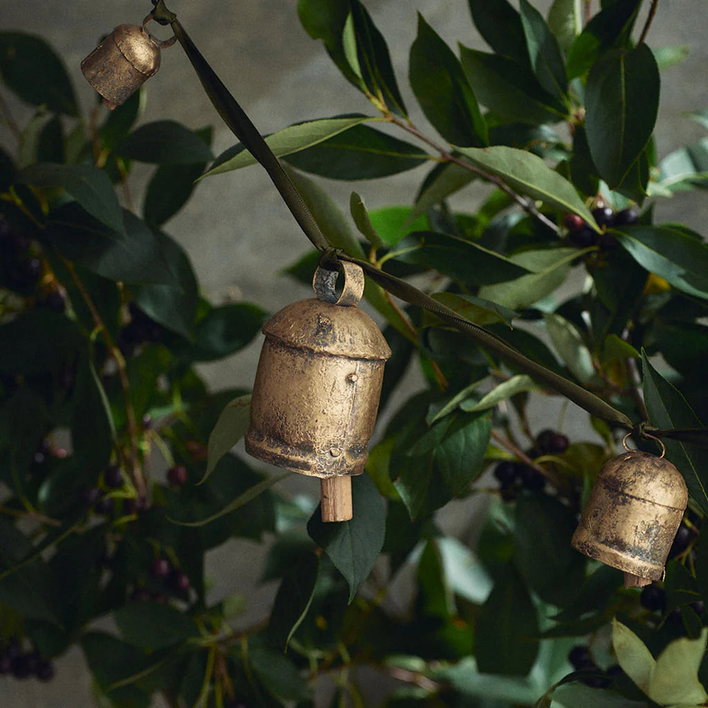 Three brass bells hanging from a branch with green leaves and small purple fruits.