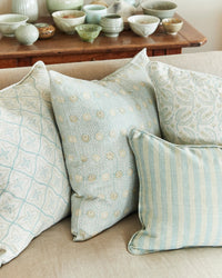 Decorative pillows with patterns on a couch, with a wooden table and ceramic bowls in the background.