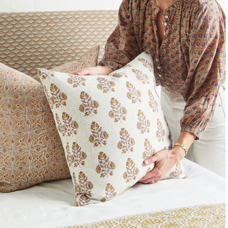 Person adjusting floral patterned pillow on bed.