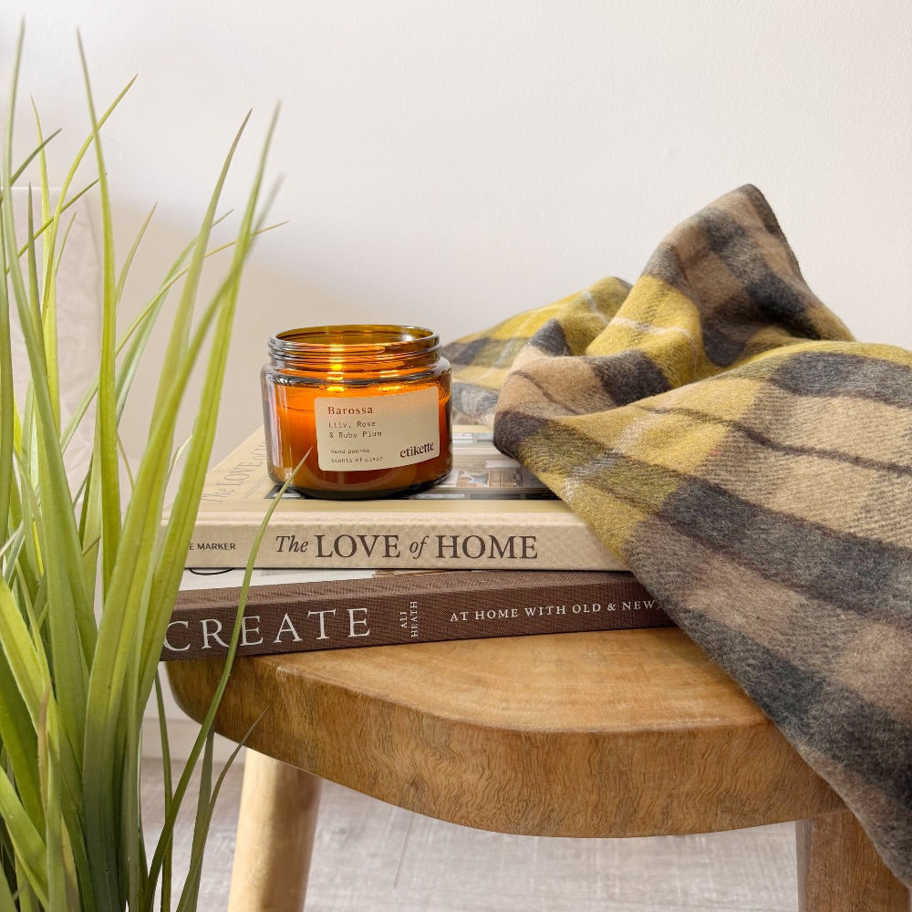 Candle on books with blanket, plant nearby.