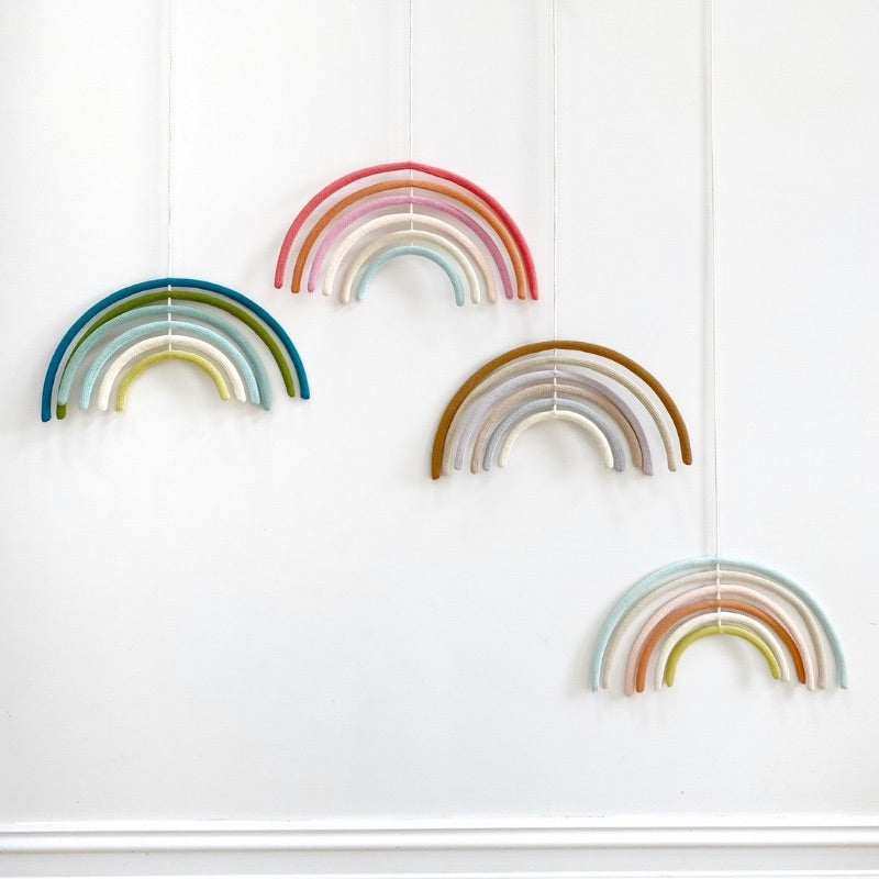Four colourful wool rainbow mobiles on white wall.