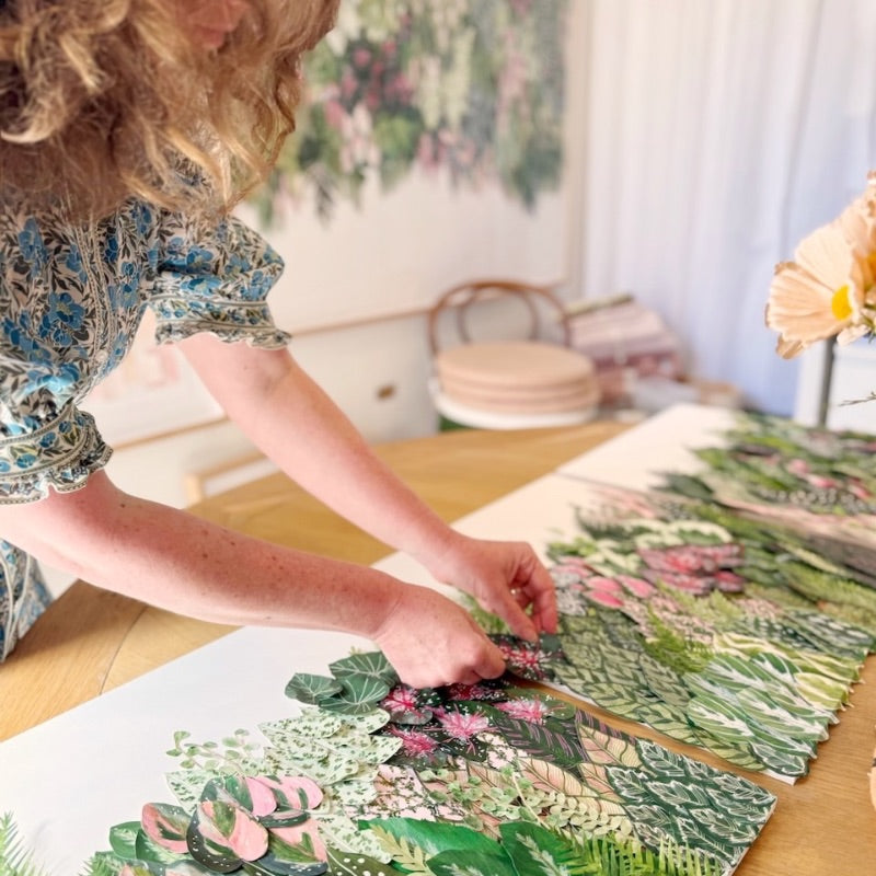 Person arranging botanical artwork on table.