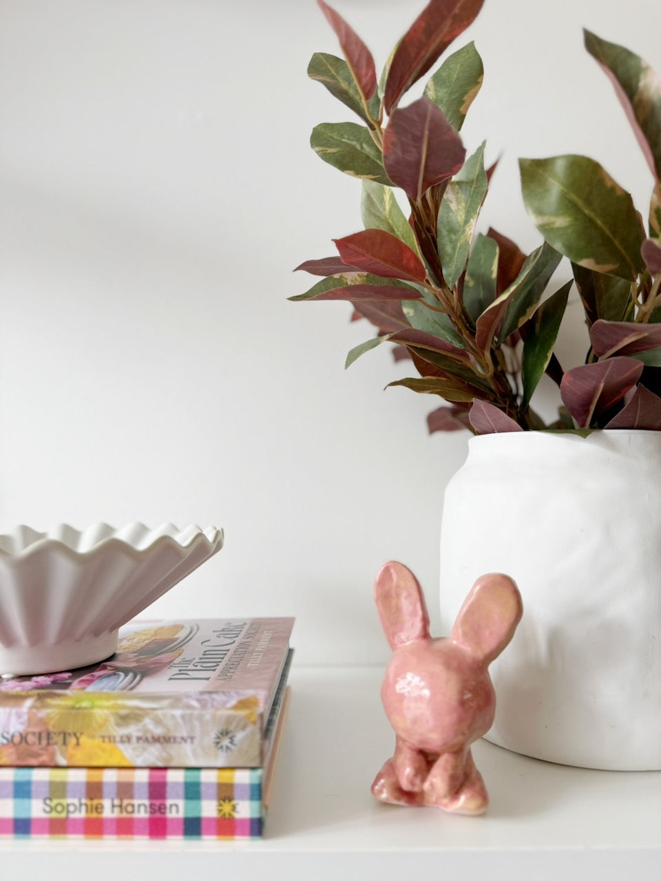 Ceramic rabbit beside books and a vase of leaves