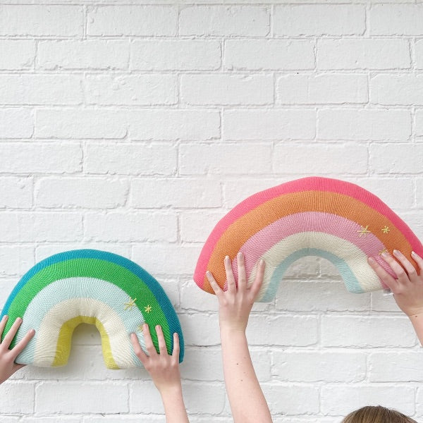 Hands holding rainbow-shaped cushions.