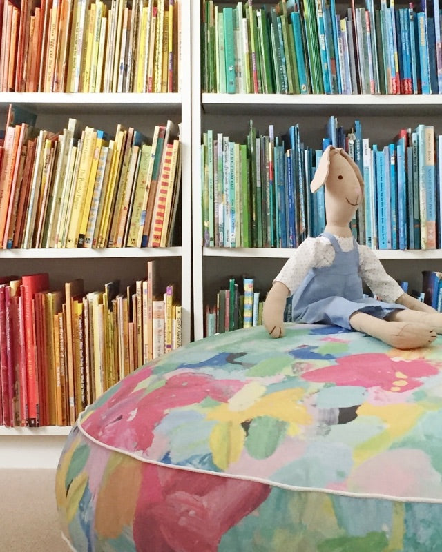 Stuffed rabbit on a colourful cushion beside a bookshelf.