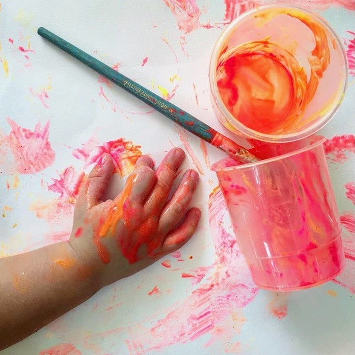Child's paint-covered hand with brush and containers.