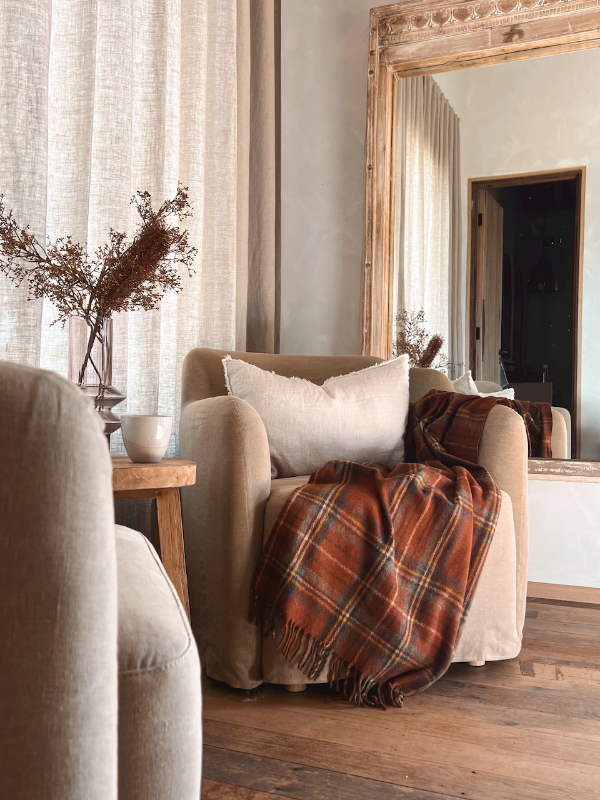 Cosy chair with plaid blanket near a mirror.