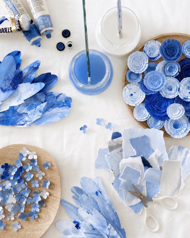 Mondocherry blue paper, materials and paint on a white table.