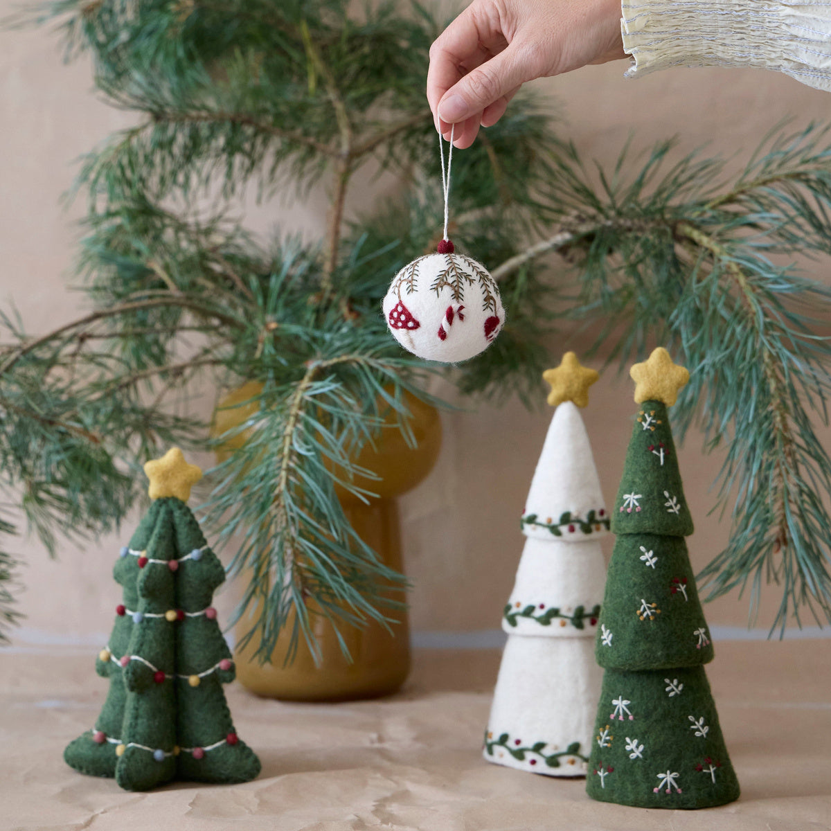 Gry & Sif — Christmas bauble — ornaments — bauble held by its loop beside evergreen branches and felt Christmas trees